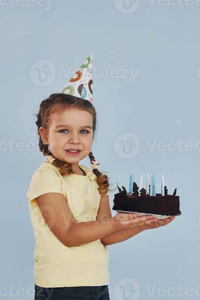 Happy little girl standing and have fun indoors at birthday party. With cake photo
