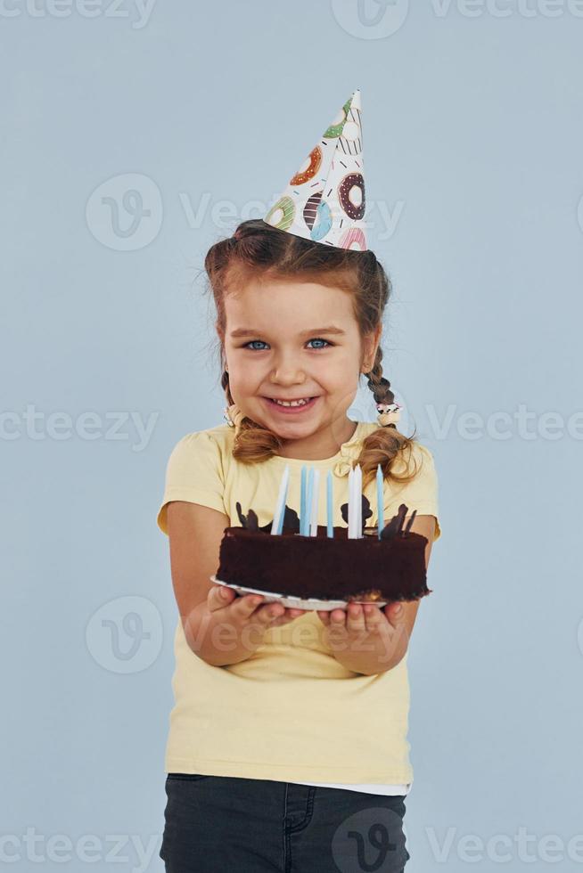 niña feliz de pie y divertirse en el interior de la fiesta de cumpleaños. con pastel foto