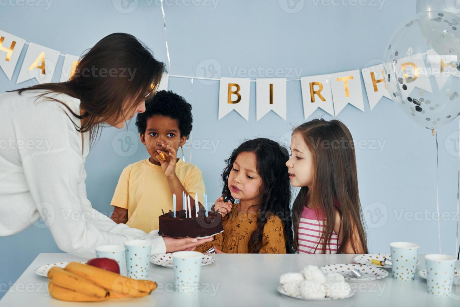 mujer sostiene pastel. los niños que celebran la fiesta de cumpleaños en el interior se divierten juntos foto