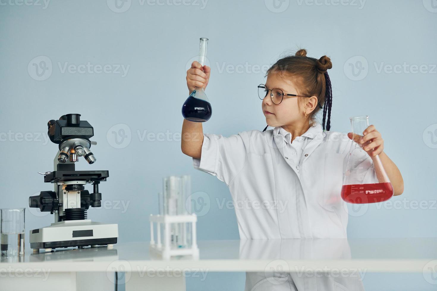 Little girl in coat playing a scientist in lab by using equipment photo