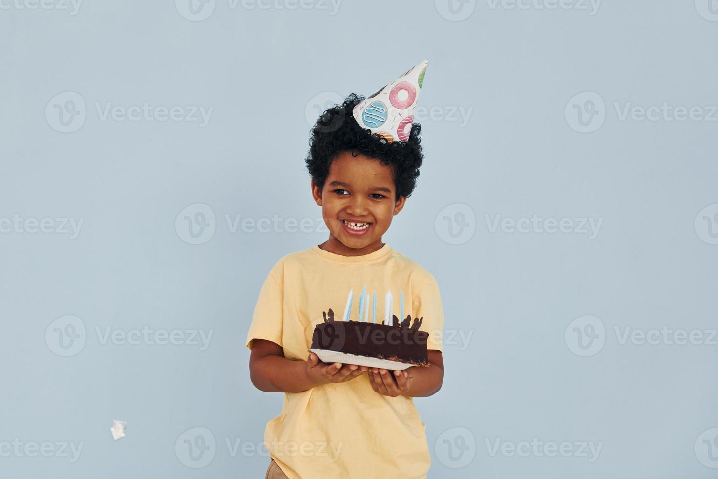 Happy little african american kid have fun indoors at birthday party holds cake photo