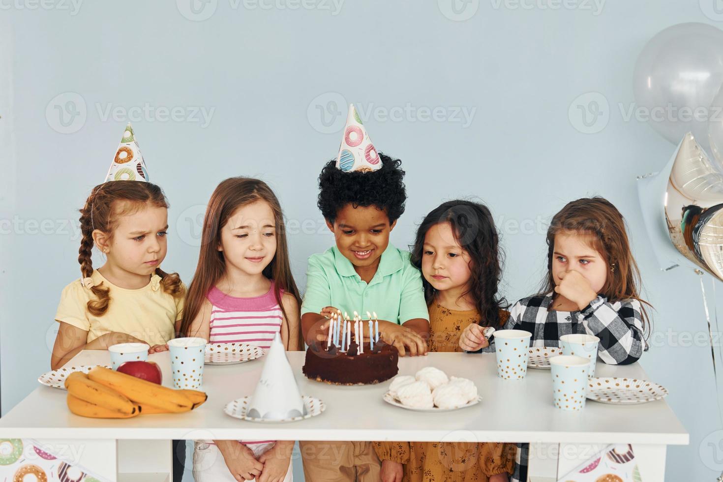 Sits by the table. Children on celebrating birthday party indoors have fun together photo
