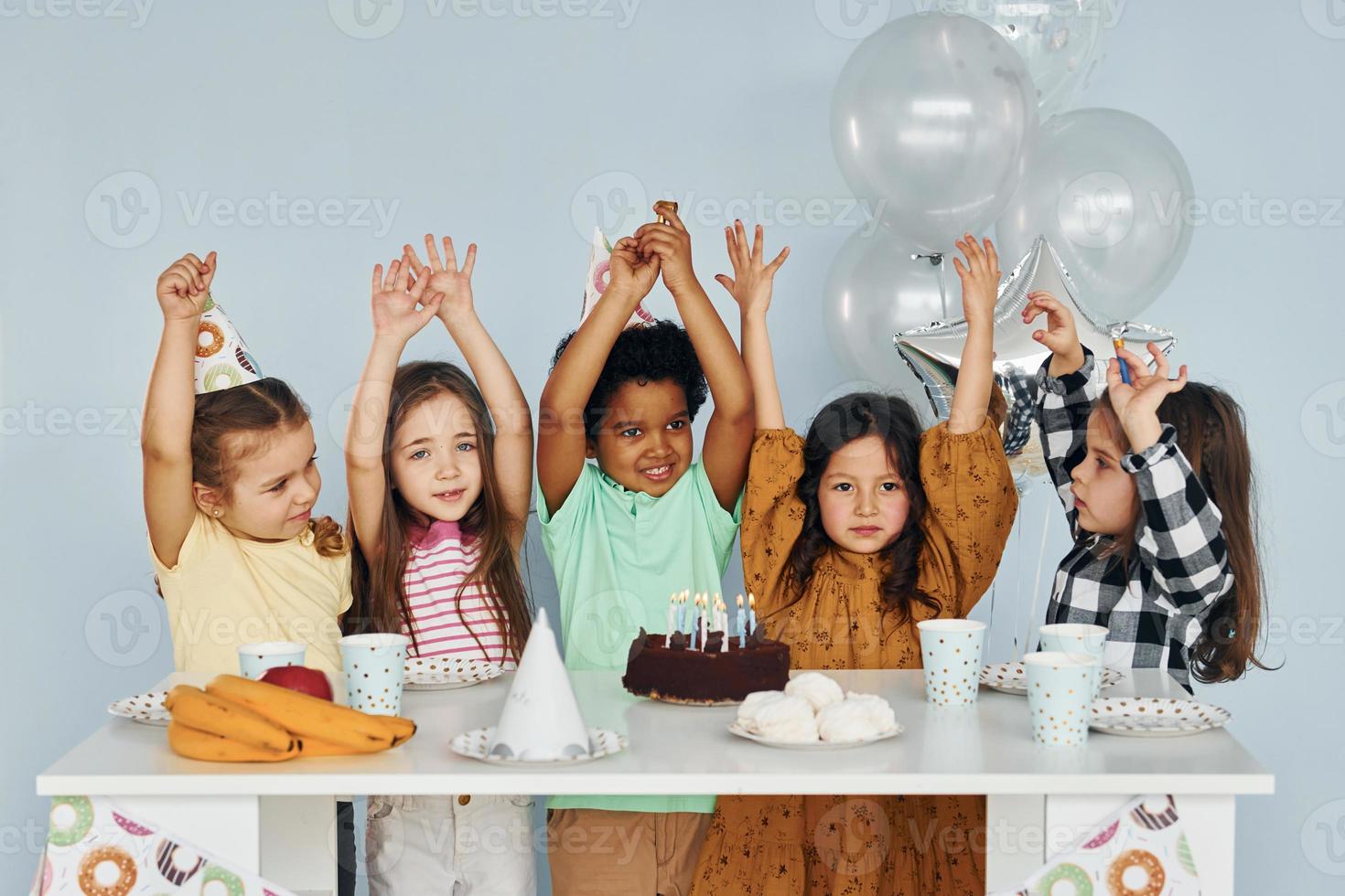 Sits by the table. Children on celebrating birthday party indoors have fun together photo