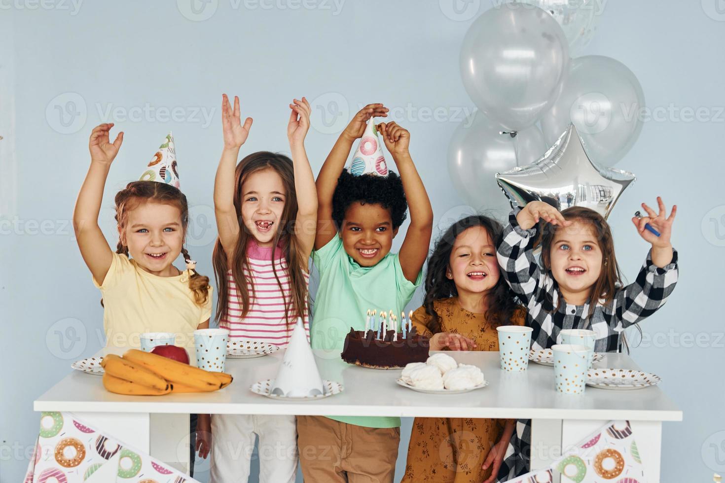 se sienta junto a la mesa. los niños que celebran la fiesta de cumpleaños en el interior se divierten juntos foto