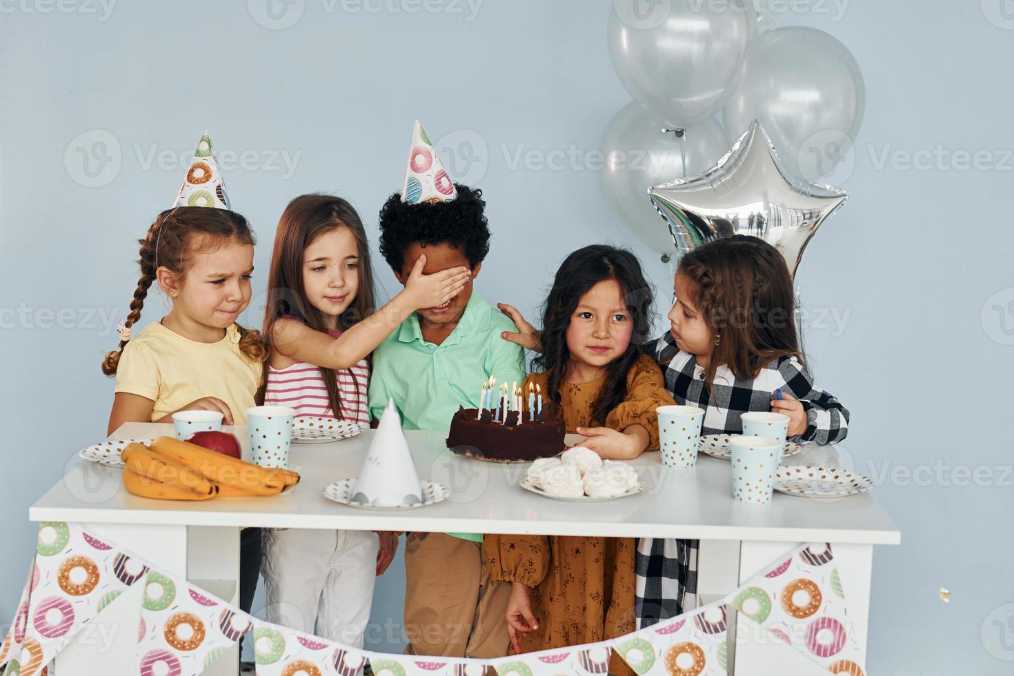 Sits by the table. Children on celebrating birthday party indoors have fun together photo