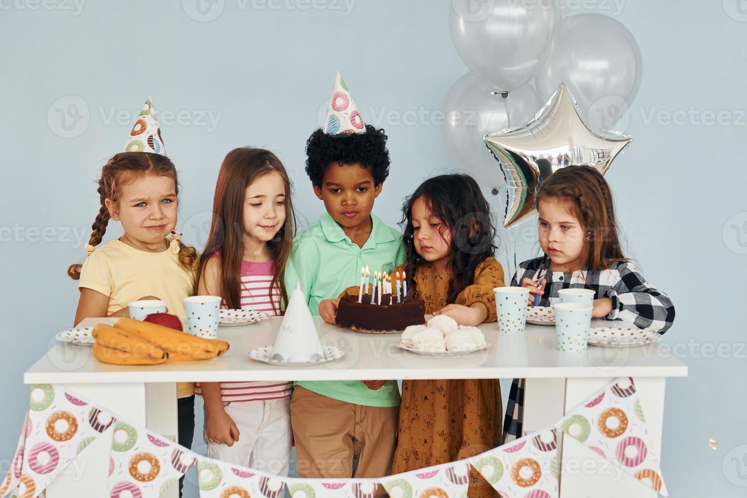 se sienta junto a la mesa. los niños que celebran la fiesta de cumpleaños en el interior se divierten juntos foto