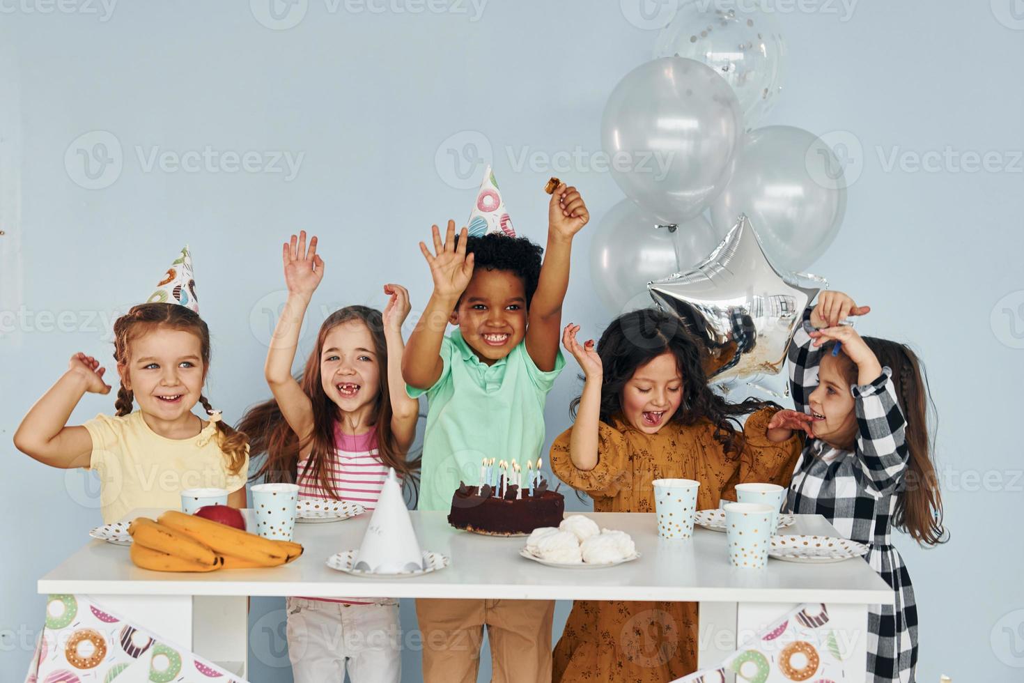 se sienta junto a la mesa. los niños que celebran la fiesta de cumpleaños en el interior se divierten juntos foto