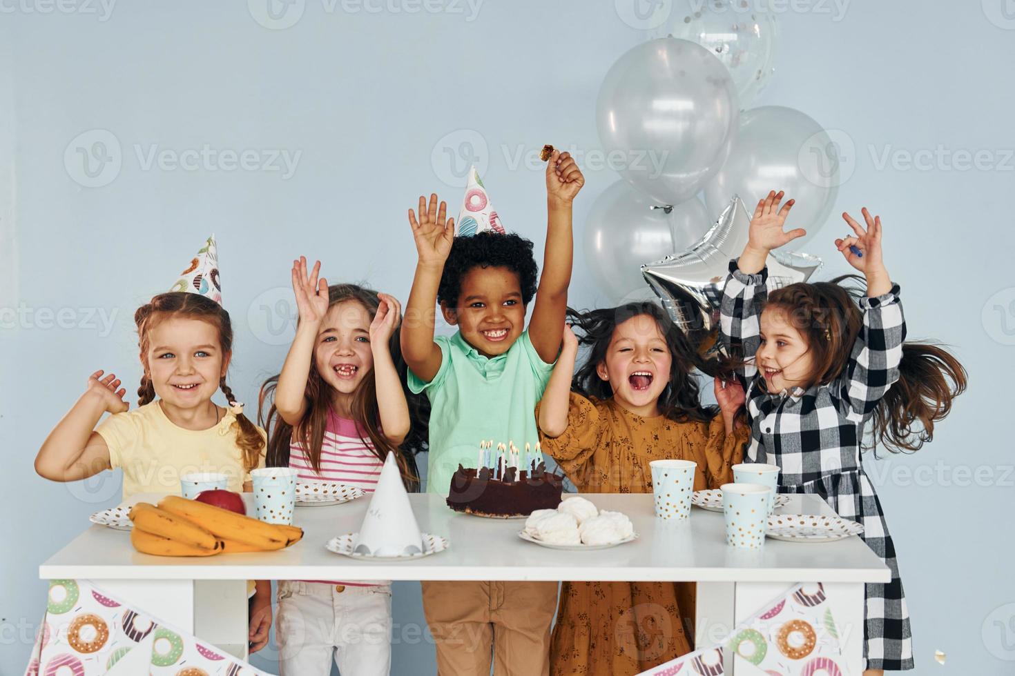 Sits by the table. Children on celebrating birthday party indoors have fun together photo