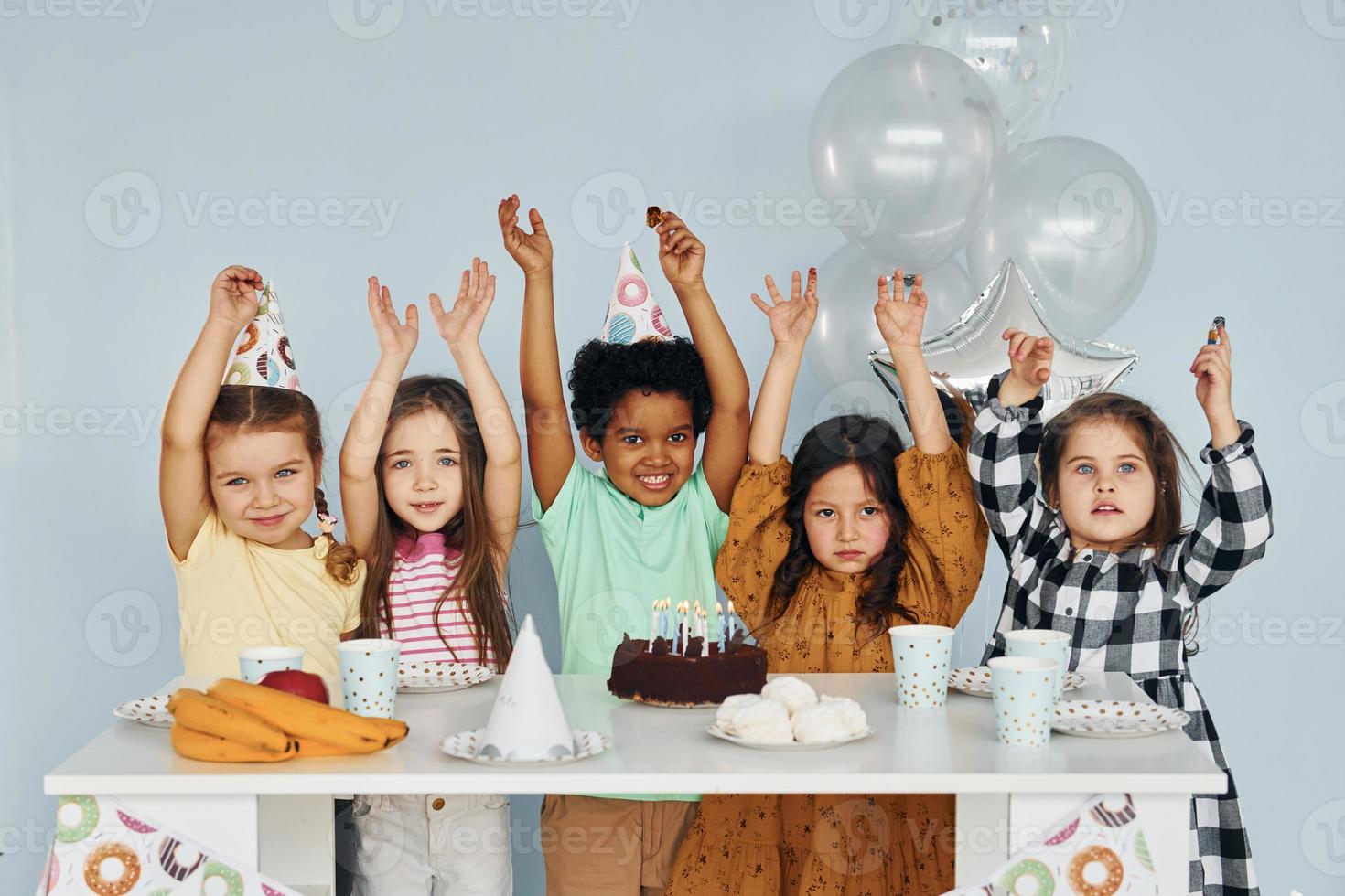 se sienta junto a la mesa. los niños que celebran la fiesta de cumpleaños en el interior se divierten juntos foto