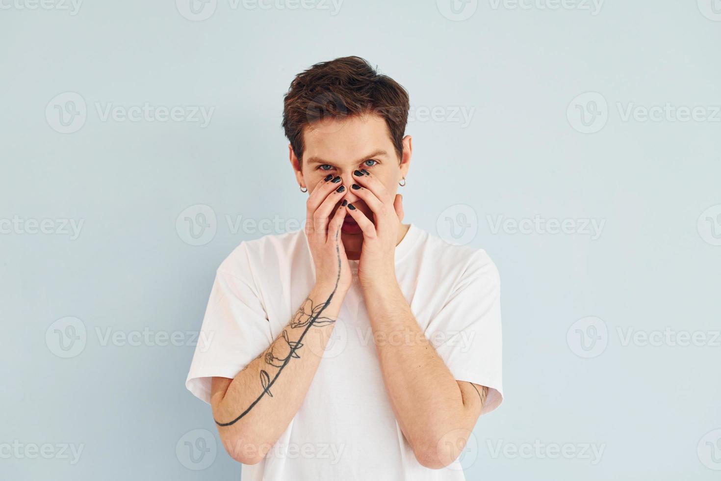 Young gay man is standing in the studio and posing for a camera. In casual white shirt photo