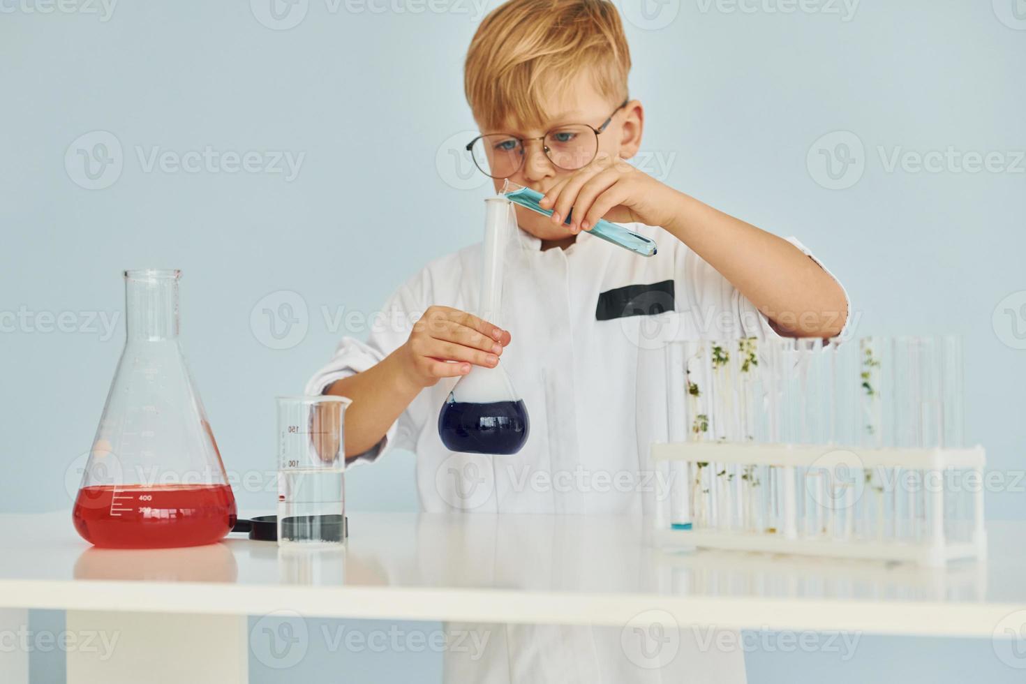 Little boy in coat playing a scientist in lab by using equipment photo