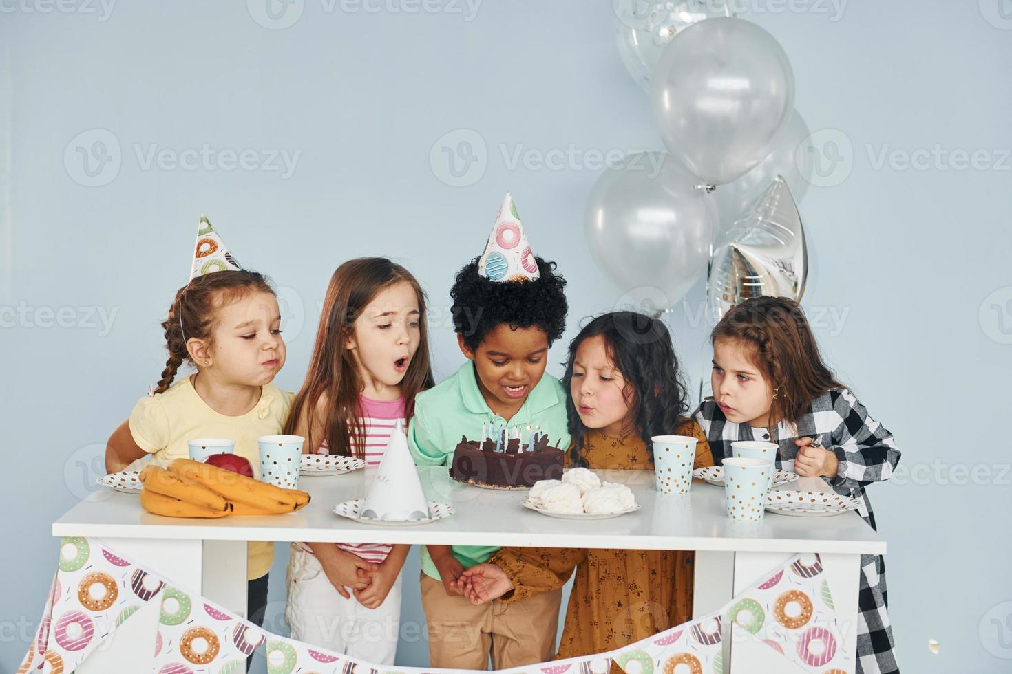 Sits by the table. Children on celebrating birthday party indoors have fun together photo