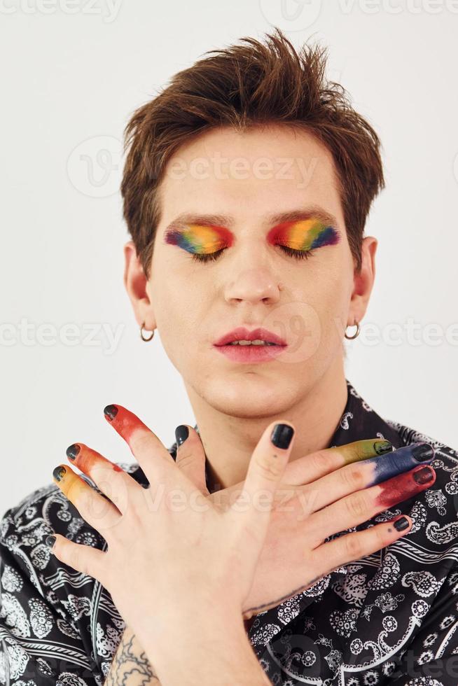 Young gay man is standing in the studio and posing for a camera. Gesturing and doing facial expressions photo