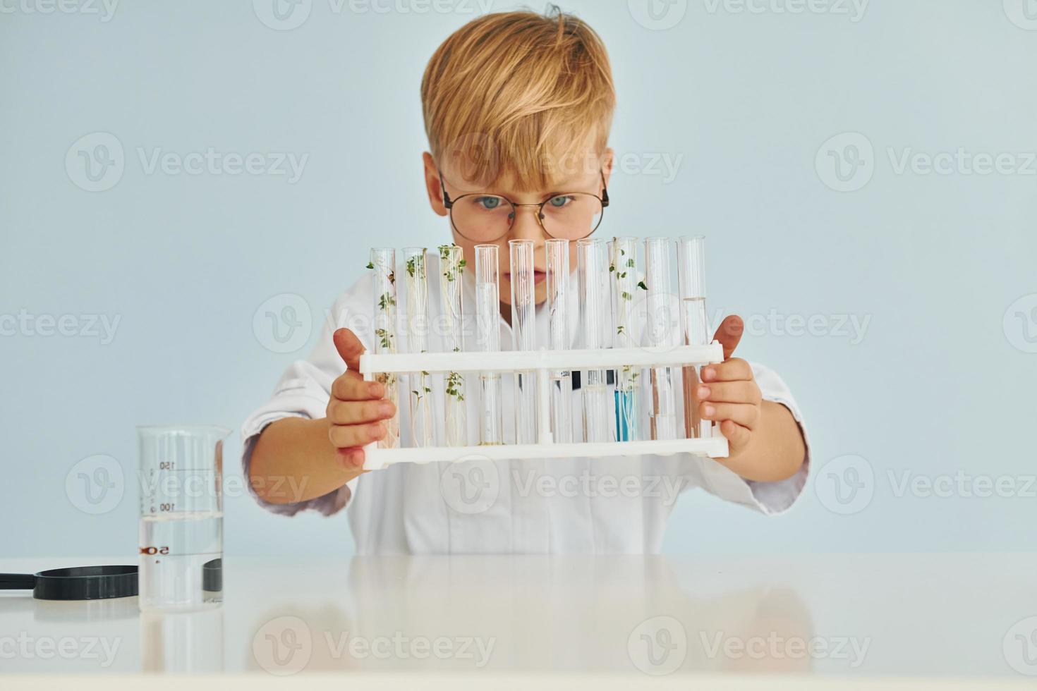 Uses test tubes. Little boy in coat playing a scientist in lab by using equipment photo
