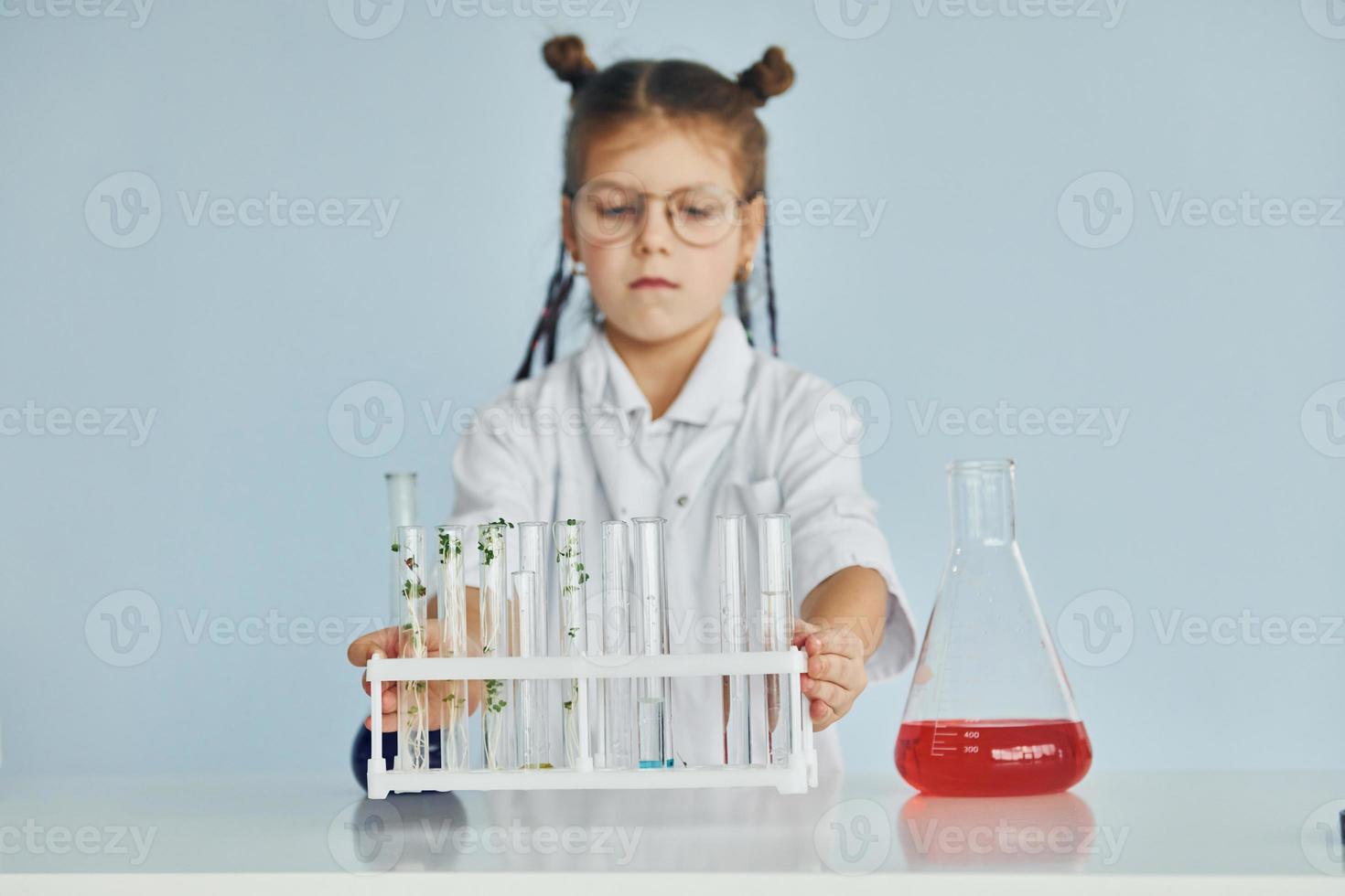 Works with test tubes. Little girl in coat playing a scientist in lab by using equipment photo