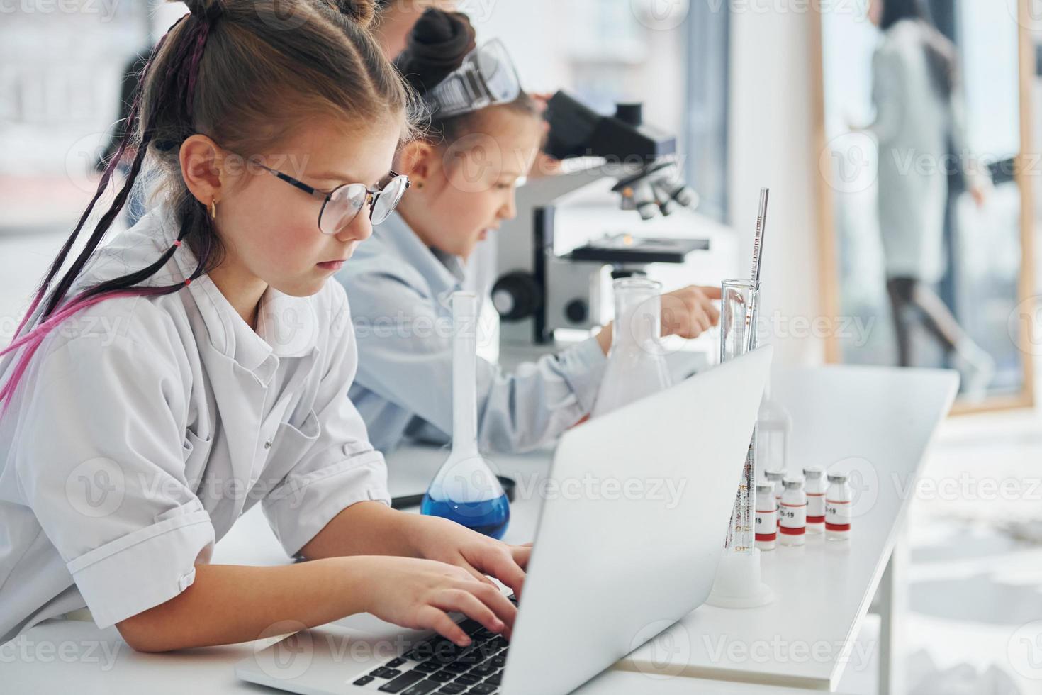 vista lateral. los niños con batas blancas juegan a los científicos en el laboratorio usando equipos foto