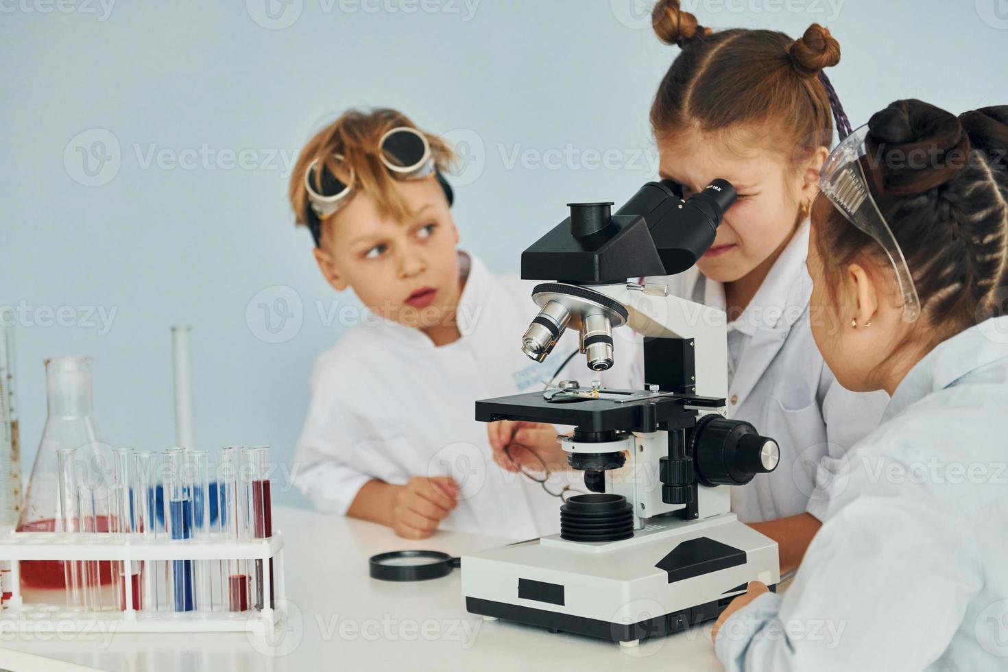 Using microscope. Children in white coats plays a scientists in lab by using equipment photo