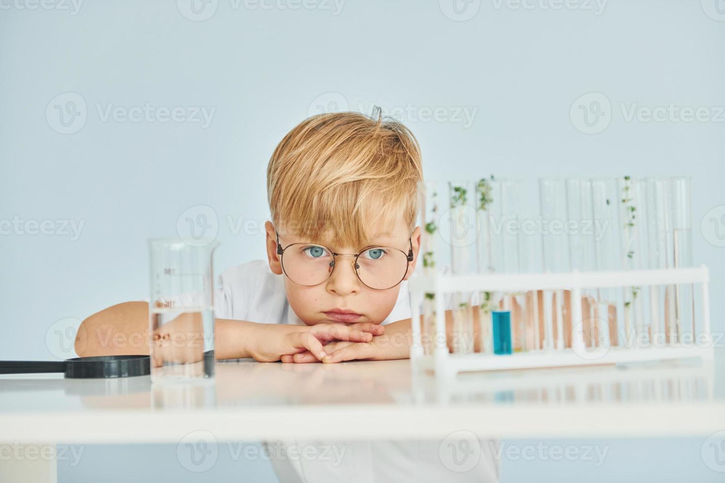 Uses test tubes. Little boy in coat playing a scientist in lab by using equipment photo