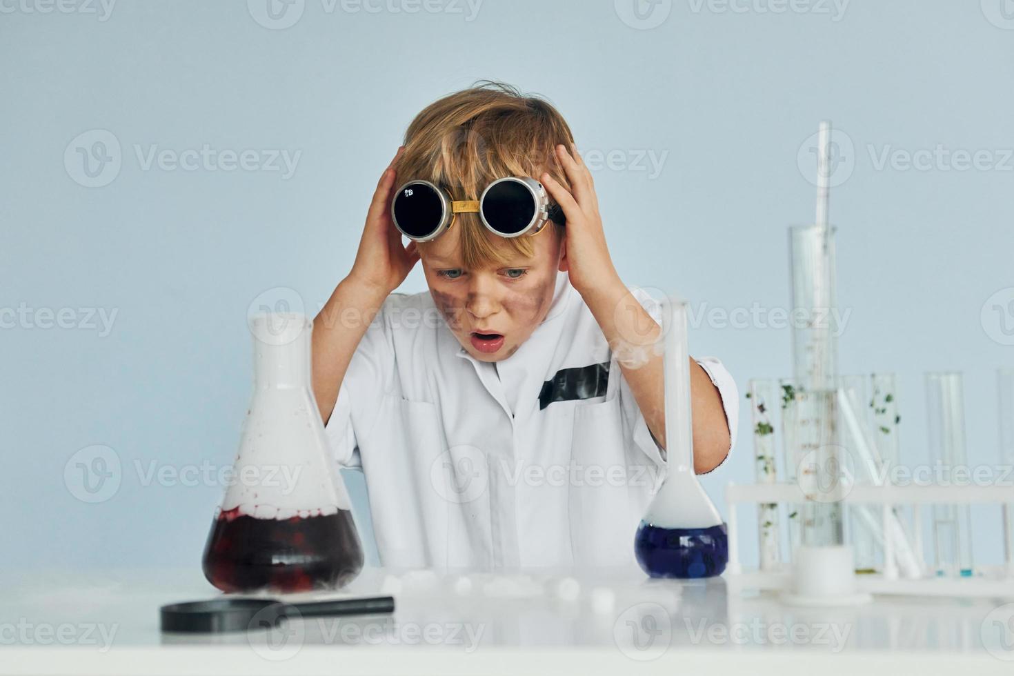 niño asustado con abrigo jugando a un científico en el laboratorio usando equipo foto