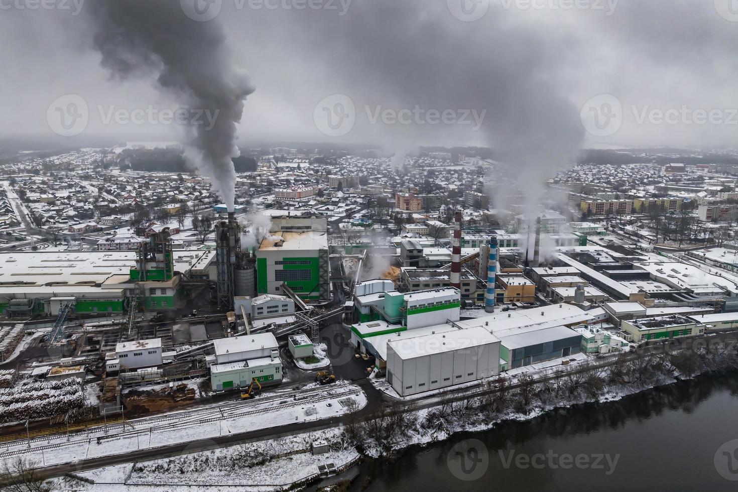 vista aérea panorámica invernal del humo oscuro de las tuberías de la empresa de carpintería con nieve. concepto de contaminación del aire y el agua. foto