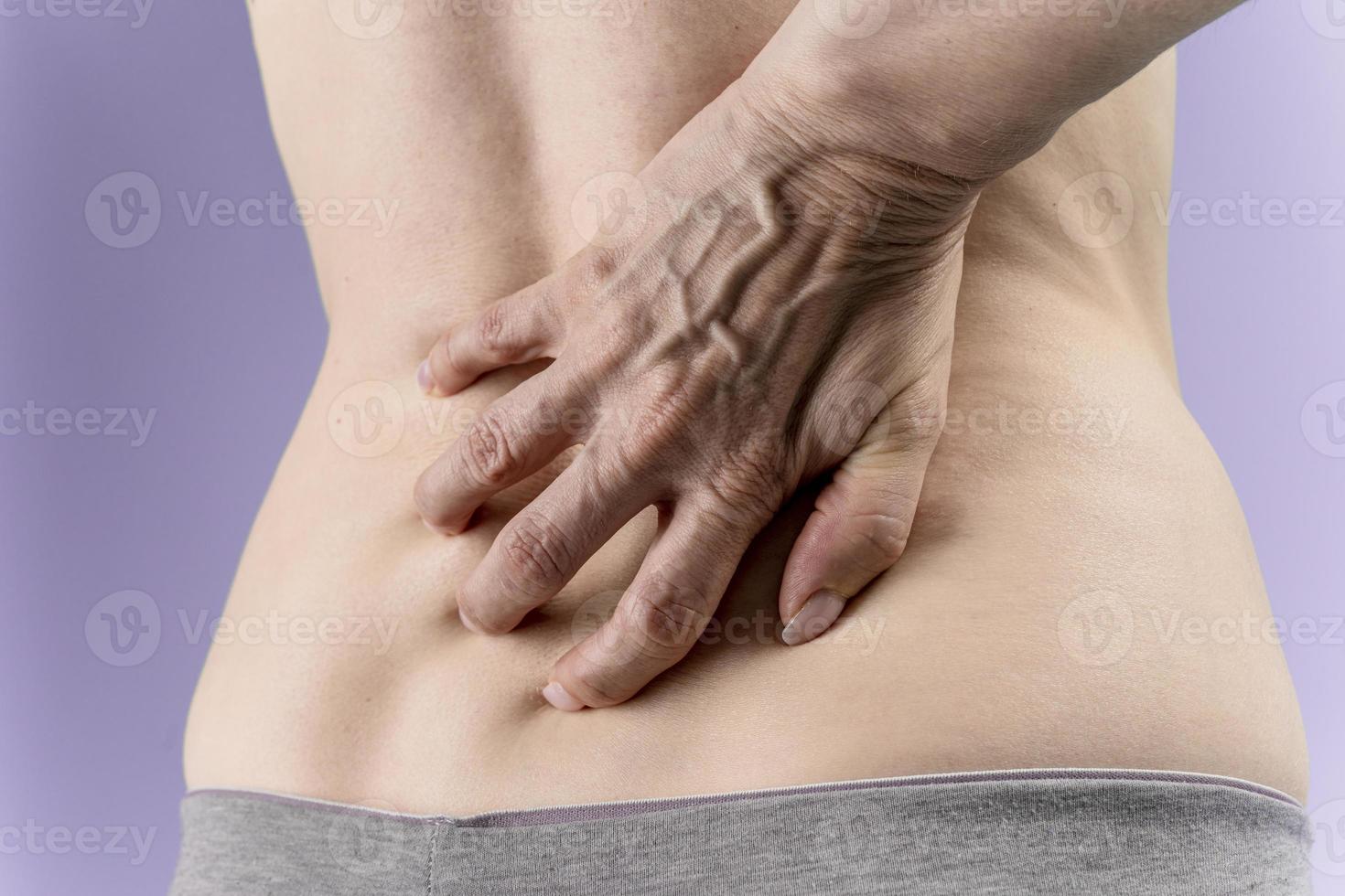 woman holding hands on her lower back feeling big pain. isolated on  purple  background photo