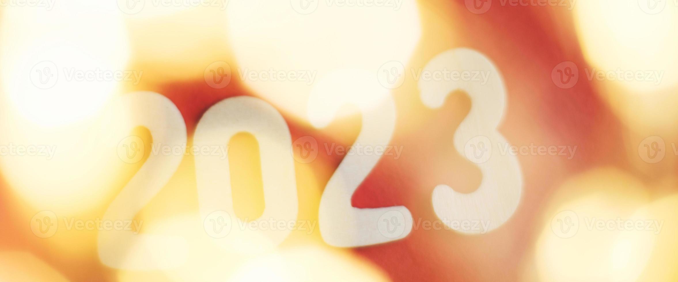 wooden number 2023 on christmas shiny gold and red background. sparkle festive blurred bokeh photo