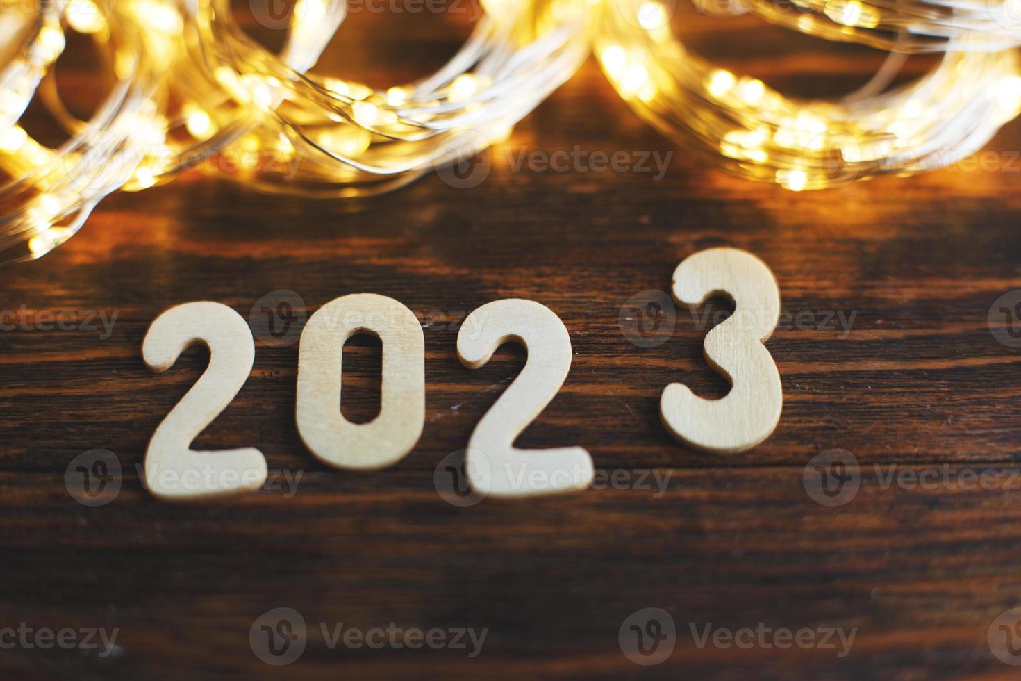 wooden number 2023 on christmas shiny wooden background. with sparkle festive gold garland photo