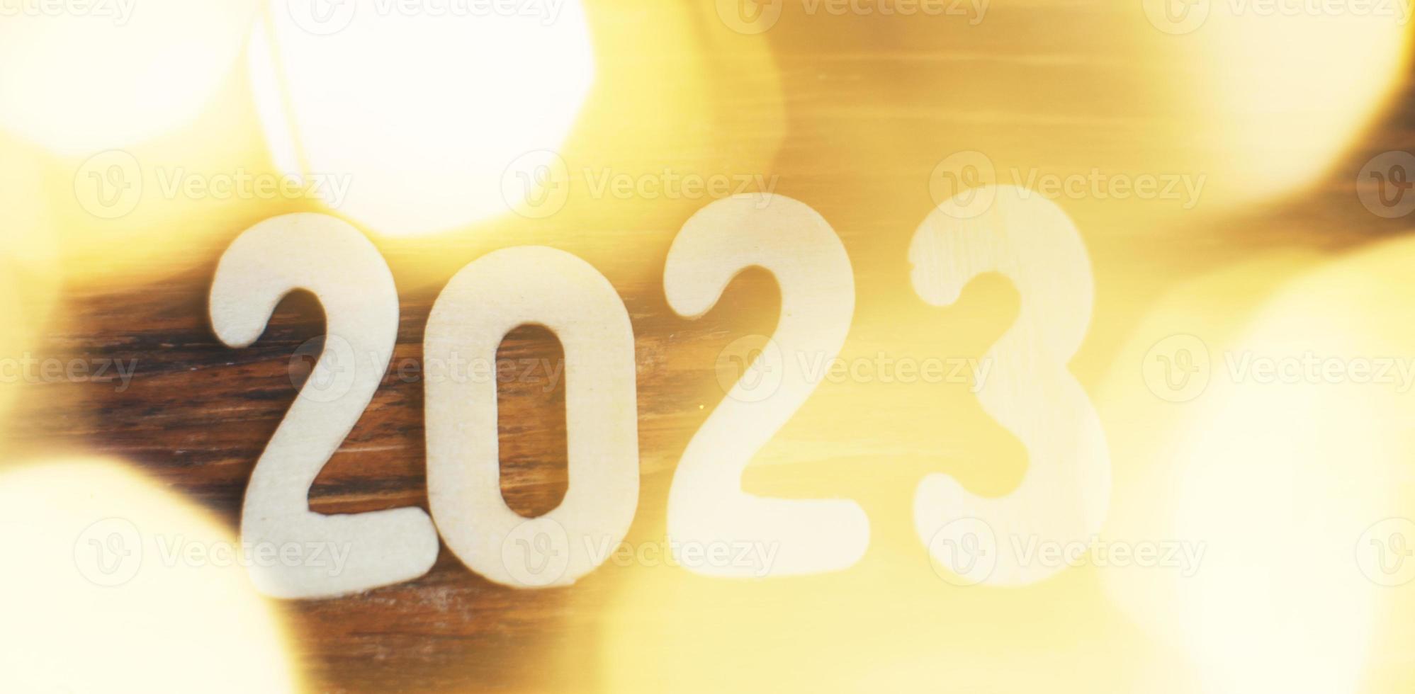 wooden number 2023 on christmas beautifull shiny gold background. sparkle festive blurred bokeh photo