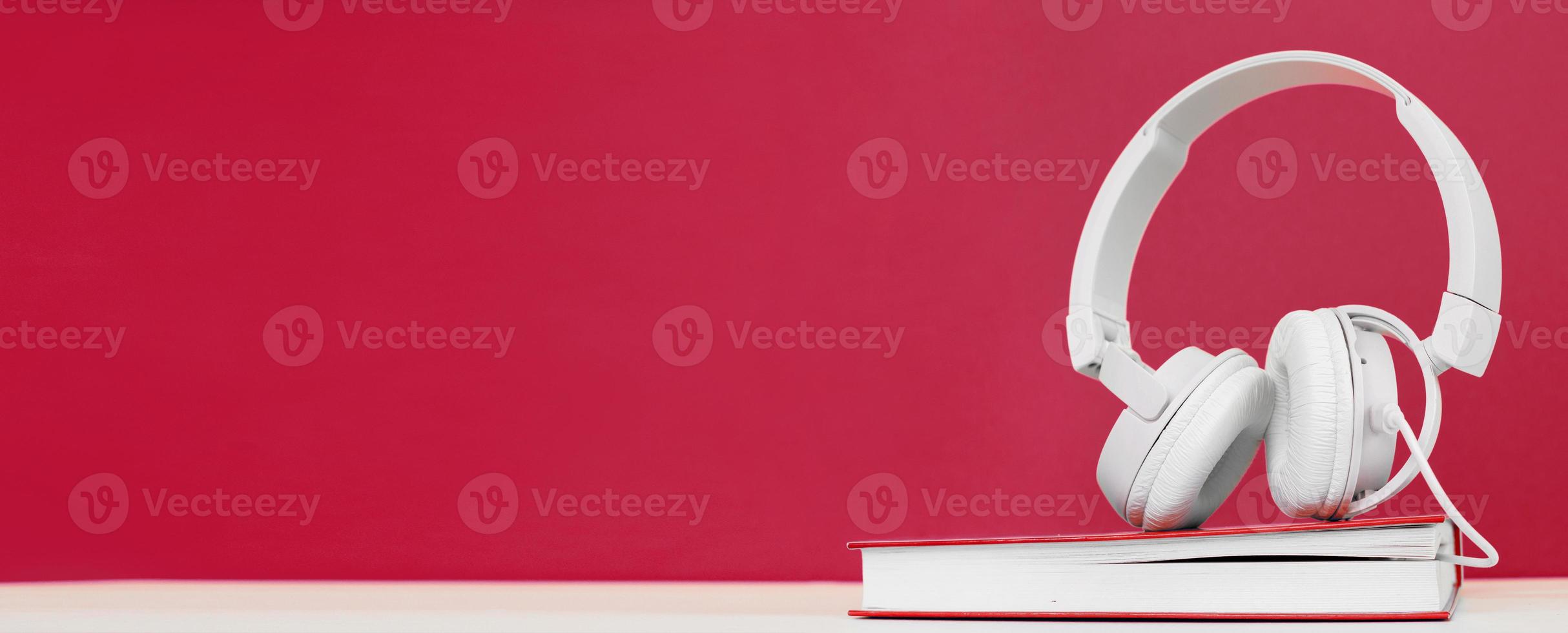 Audio book concept with headphones and a book on a viva magenta background. Listening to a book. photo