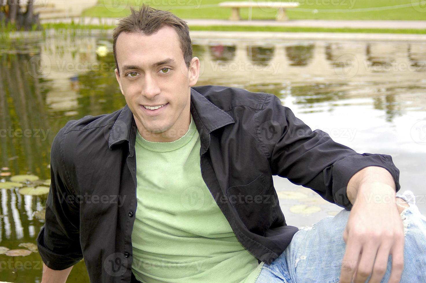 Sexy and  handsome young man smiling as he sits in front of a reflection pond. photo