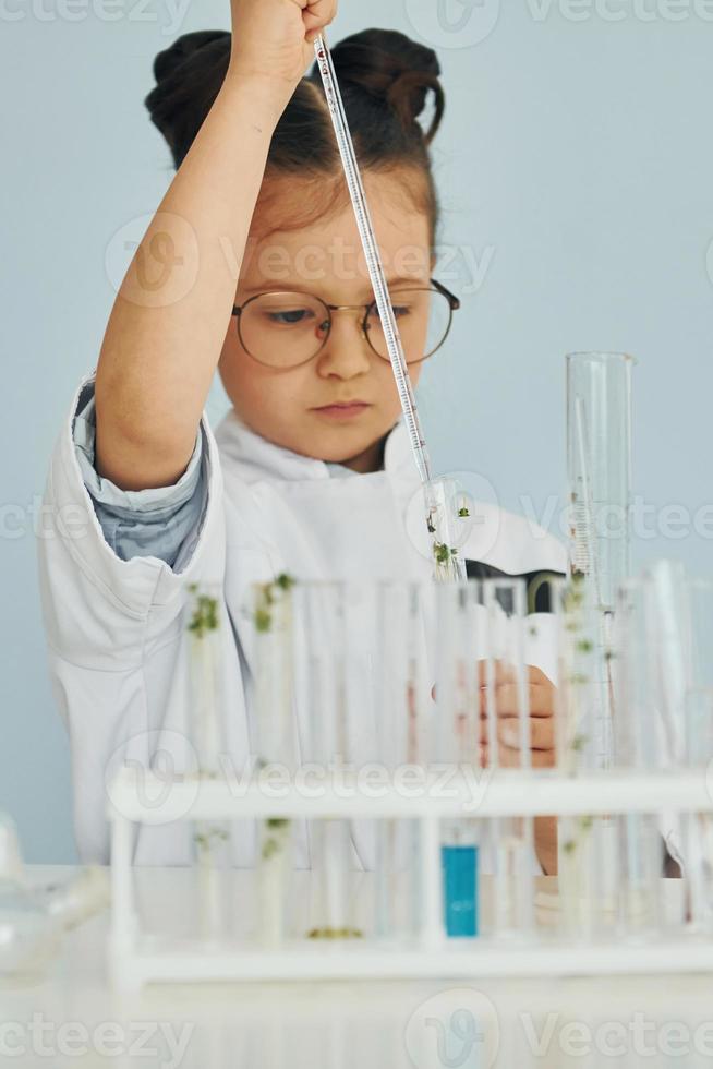 Workes with liquid that is in test tubes. Little girl in coat playing a scientist in lab by using equipment photo