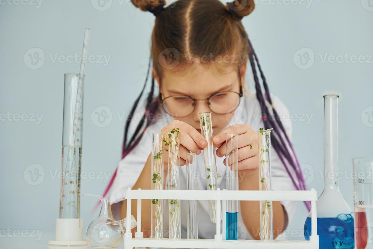 Workes with liquid that is in test tubes. Little girl in coat playing a scientist in lab by using equipment photo