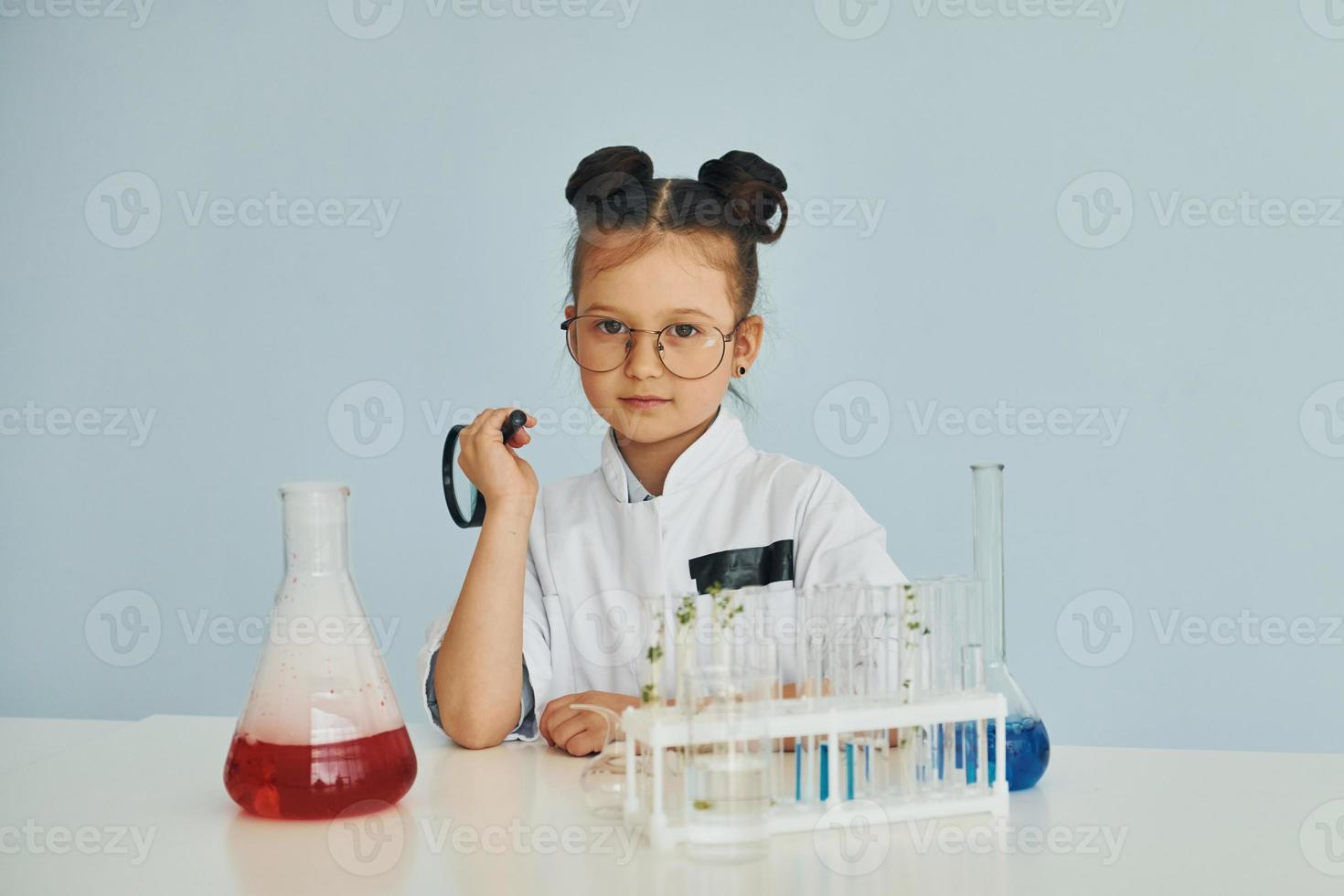 Works with test tubes. Little girl in coat playing a scientist in lab by using equipment photo