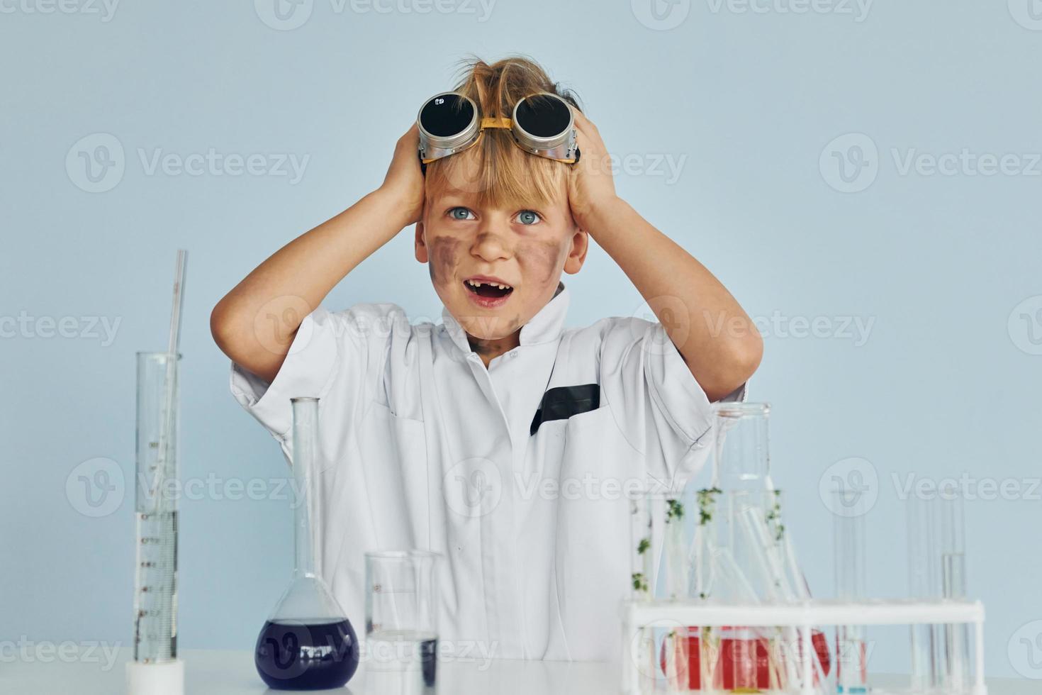 Scared little boy in coat playing a scientist in lab by using equipment photo