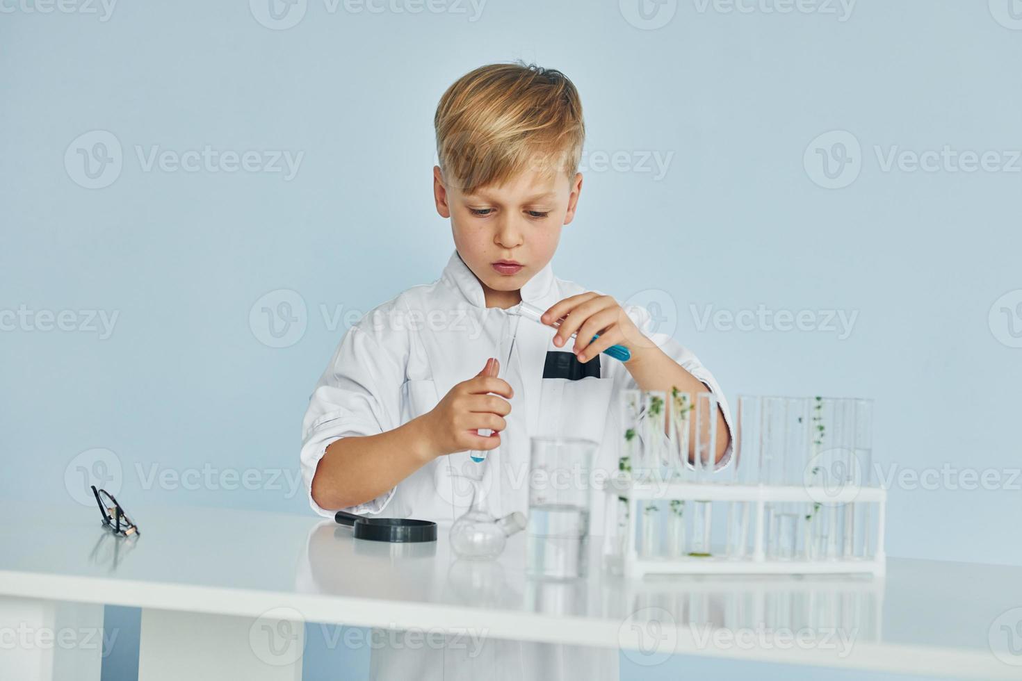 Uses test tubes. Little boy in coat playing a scientist in lab by using equipment photo