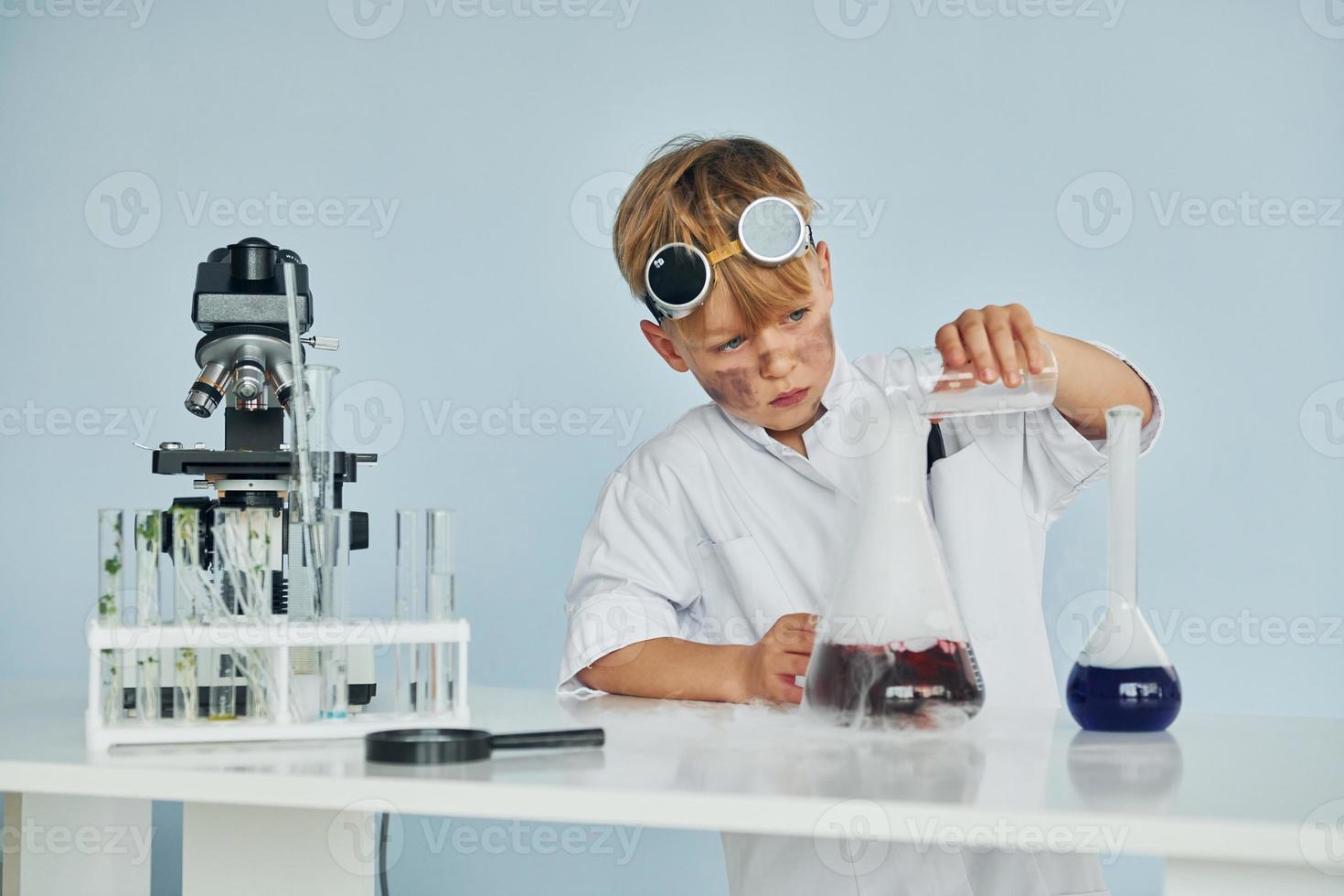 Little boy in coat playing a scientist in lab by using equipment photo