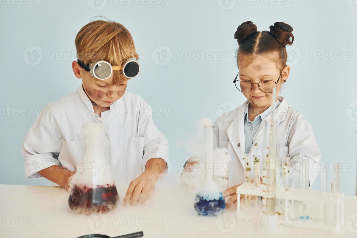 Girl with boy working together. Children in white coats plays a scientists in lab by using equipment photo