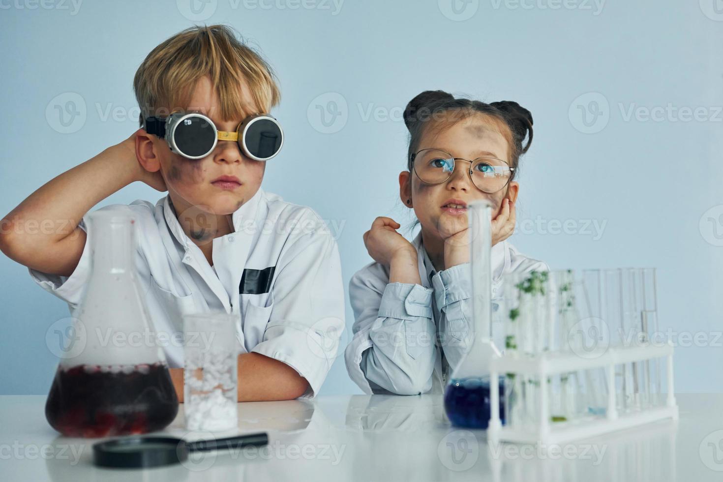 Girl with boy working together. Children in white coats plays a scientists in lab by using equipment photo