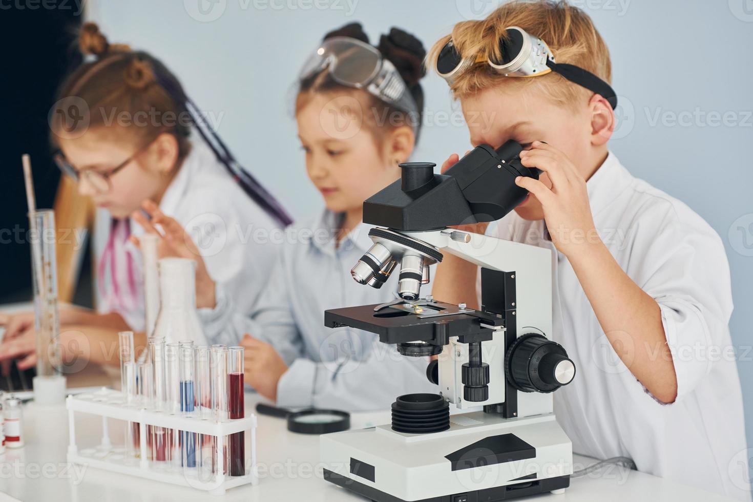 Using microscope. Children in white coats plays a scientists in lab by using equipment photo