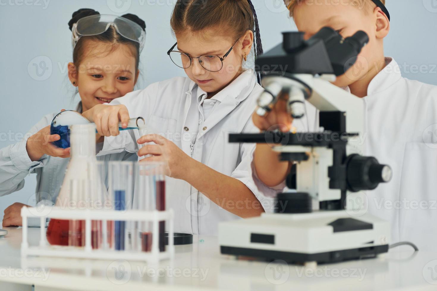 Using microscope. Children in white coats plays a scientists in lab by using equipment photo