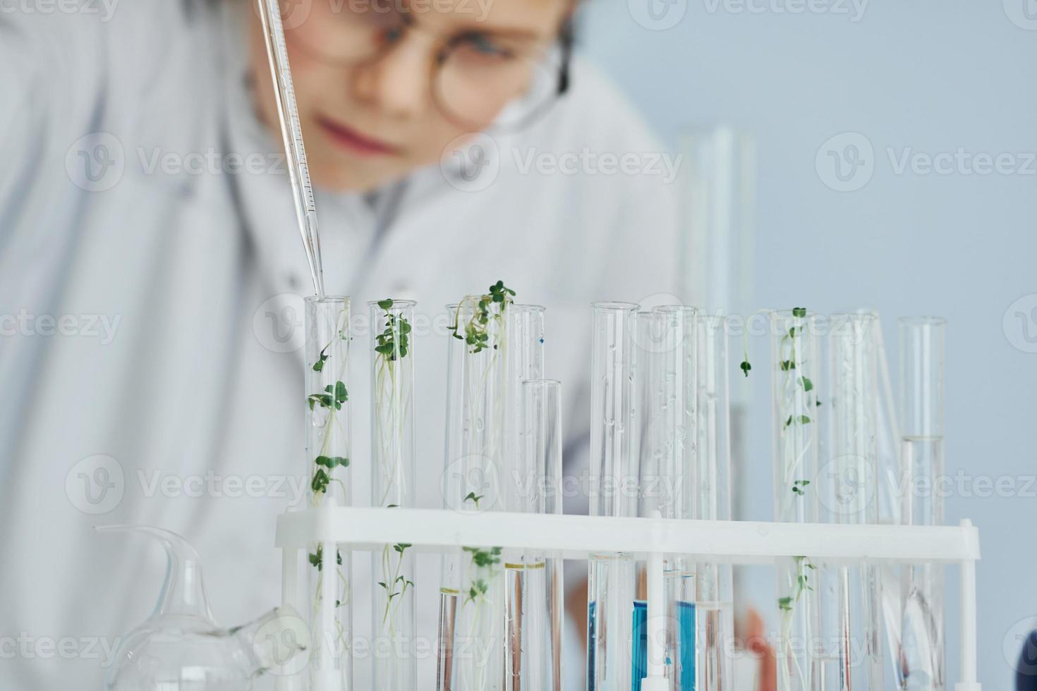 Works with test tubes. Little girl in coat playing a scientist in lab by using equipment photo