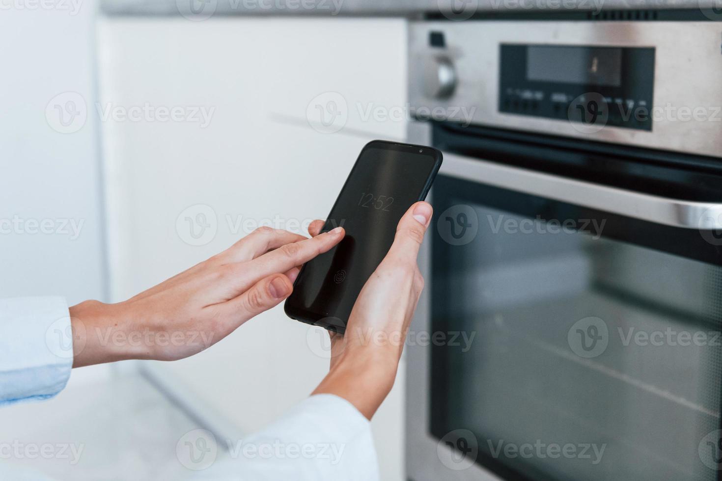 la mujer joven está adentro en la habitación de la casa inteligente controlando el horno foto