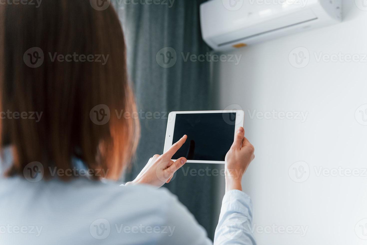 Controlling conditioner by tablet. Young woman is indoors in room of modern house at daytime photo