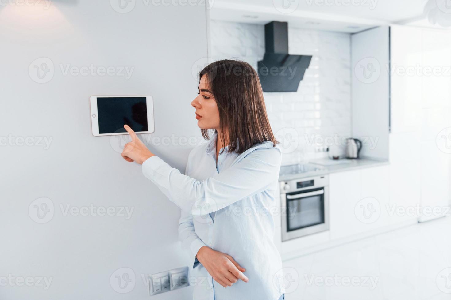 utiliza una tableta que se monta en la pared. la mujer joven está adentro en la habitación de la casa inteligente durante el día foto