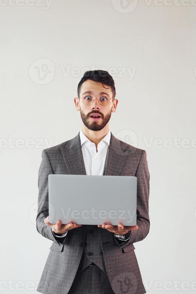 With laptop in hands. Young stylish businessman in suit indoors. Conception of success photo