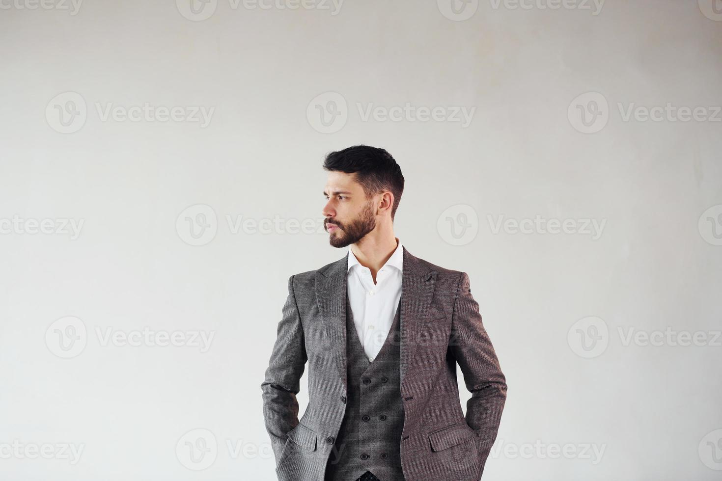 Posing for a camera against white background. Young stylish businessman in suit indoors photo