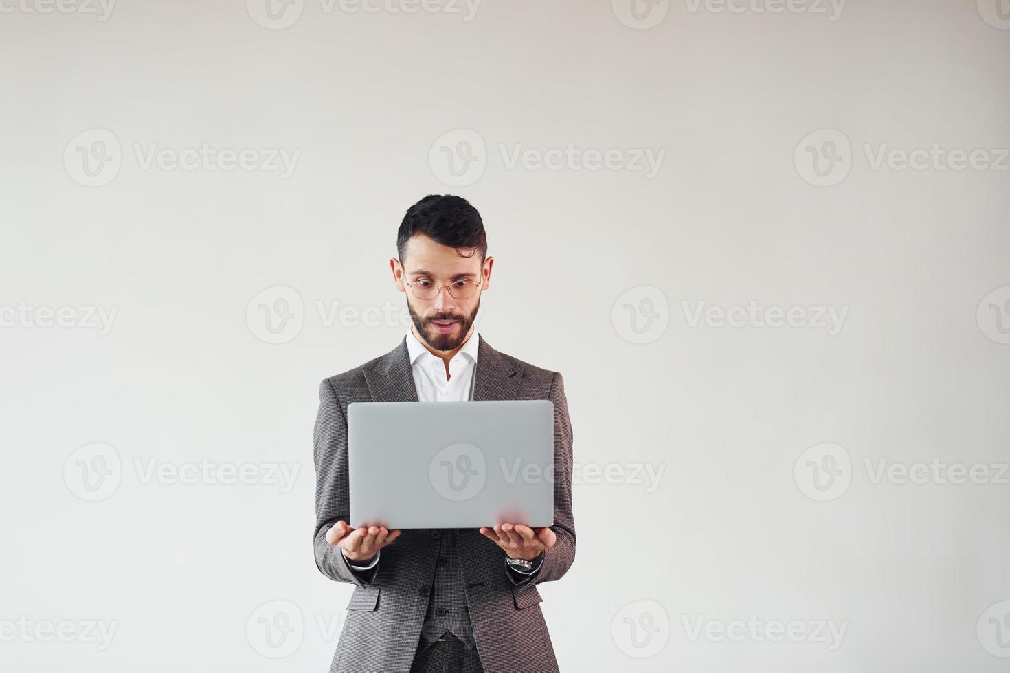 Uses laptop. Young stylish businessman in suit indoors. Conception of success photo