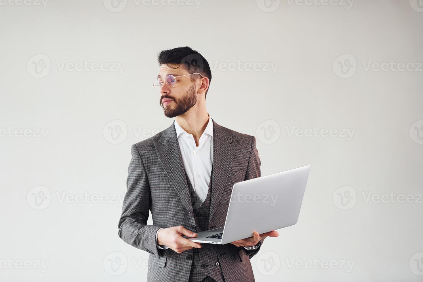 With laptop in hands. Young stylish businessman in suit indoors. Conception of success photo