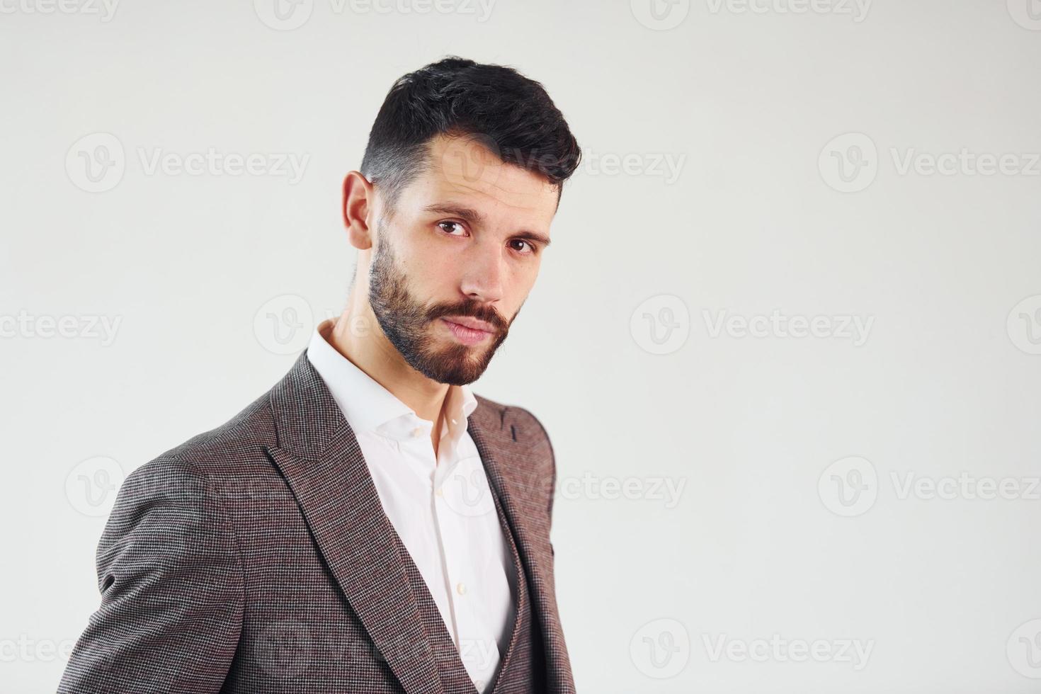 Posing for a camera against white background. Young stylish businessman in suit indoors photo