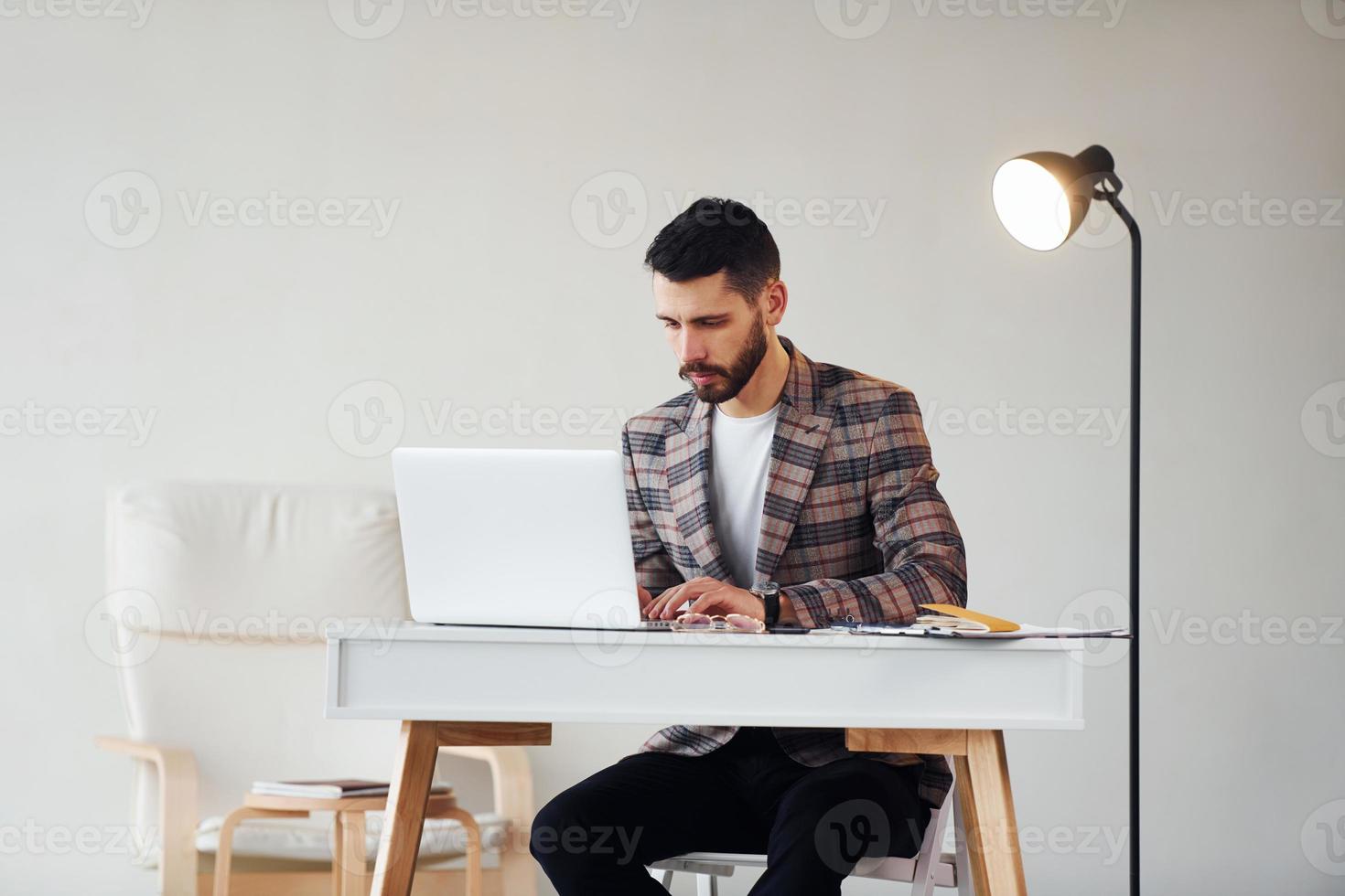 Uses laptop. Young stylish businessman in suit indoors. Conception of success photo